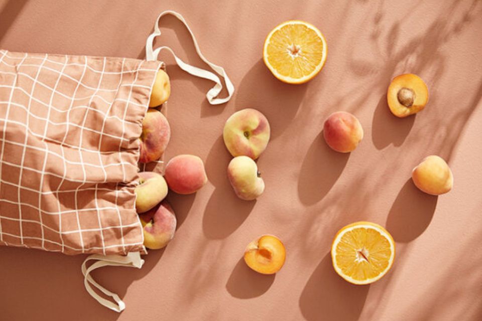 Eco-friendly gifts for children featuring fresh peaches and oranges in a reusable cloth bag.